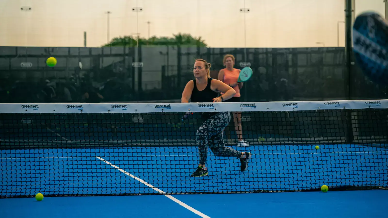 Social Sports Society Announces New Padel Facility at Brabazon Bristol. Woman running after a ball with her racket raised during a Padel game.