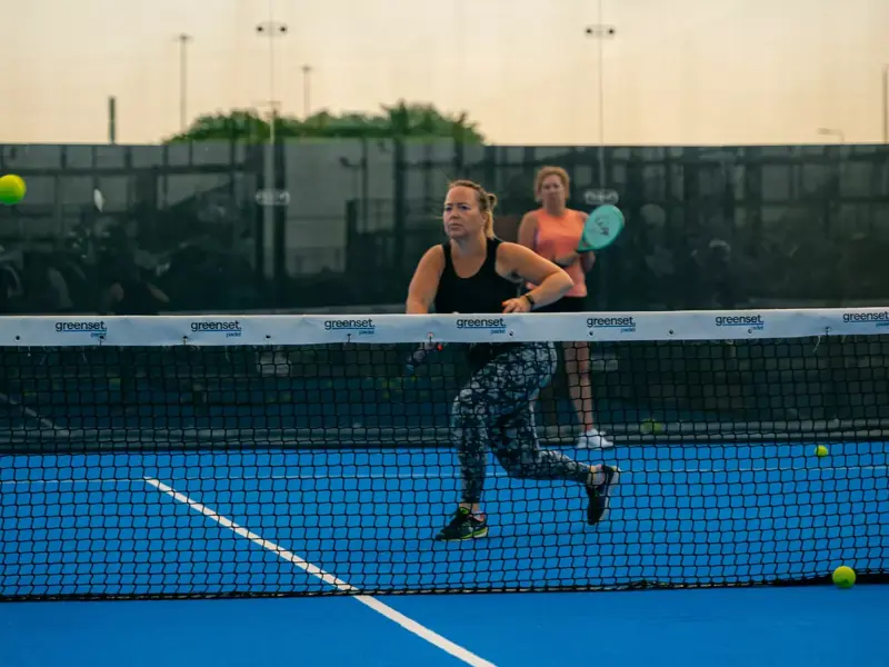 Social Sports Society Announces New Padel Facility at Brabazon Bristol. Woman running after a ball with her racket raised during a Padel game.